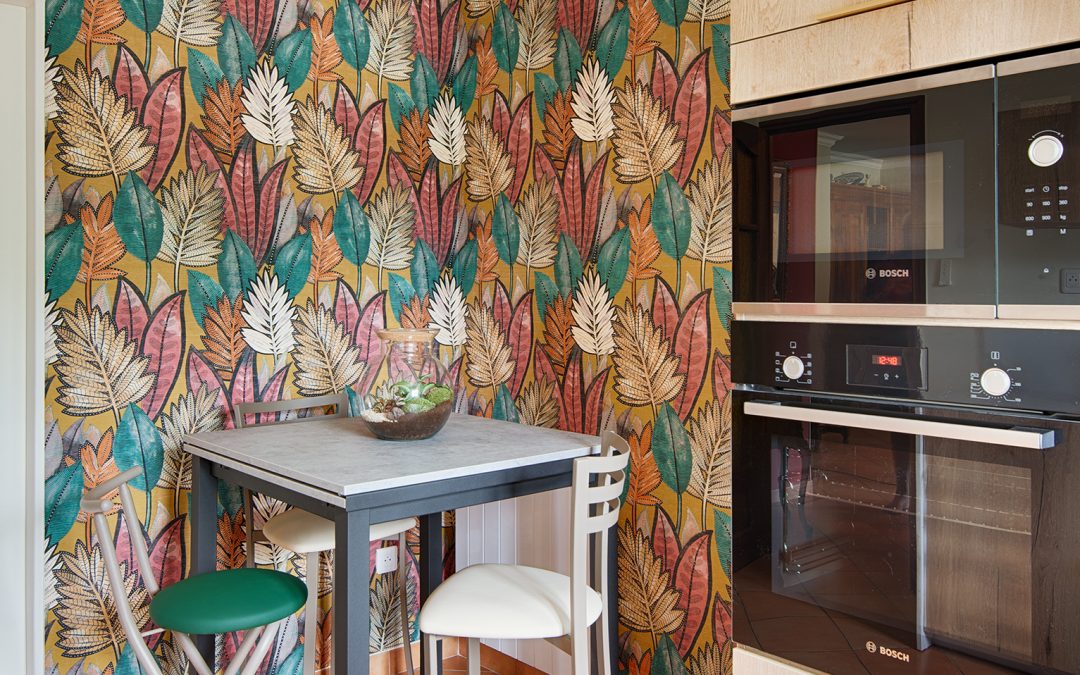 Vue coin repas avec colonne four, table snack et papier peint feuillage coloré, par Kty.L, décoratrice d'intérieur, UFDI, Avignon et Nîmes